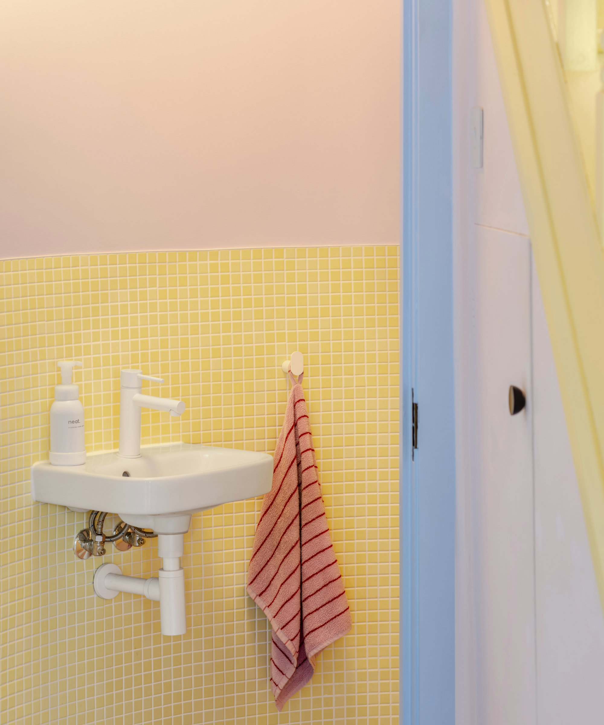 Bathroom with pastel yellow tiles, white sink and pastel pink wall