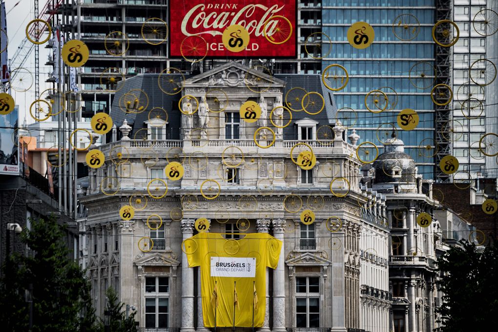 Tinsels with bicycle wheels hanging in a street with a giant Yellow Jersey hanging on a facade in Brussels centre