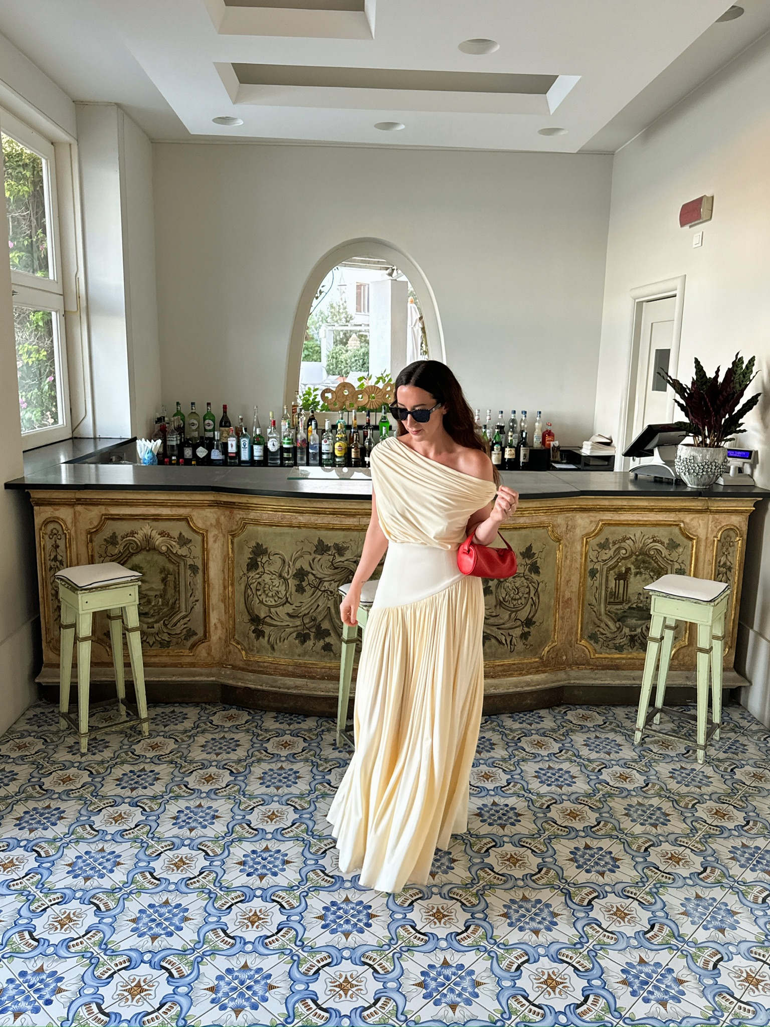 Caitlin Burke wearing a cream-colored draped gown and carrying a red The Row &#039;90s bag.