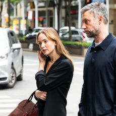 Jennifer Lawrence walking with her husband, wearing a black oversized blazer with a lace-trimmed white slip skirt, strappy nude high-heel sandals, and a croc The Row bag