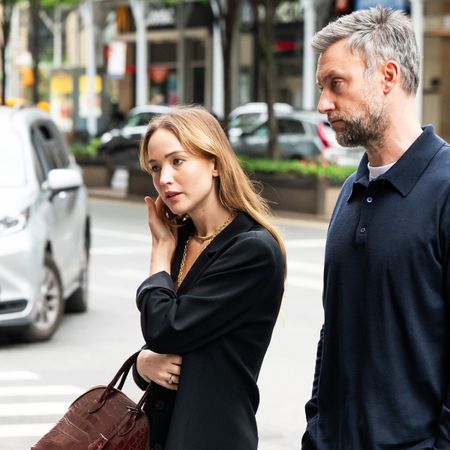 Jennifer Lawrence walking with her husband, wearing a black oversized blazer with a lace-trimmed white slip skirt, strappy nude high-heel sandals, and a croc The Row bag