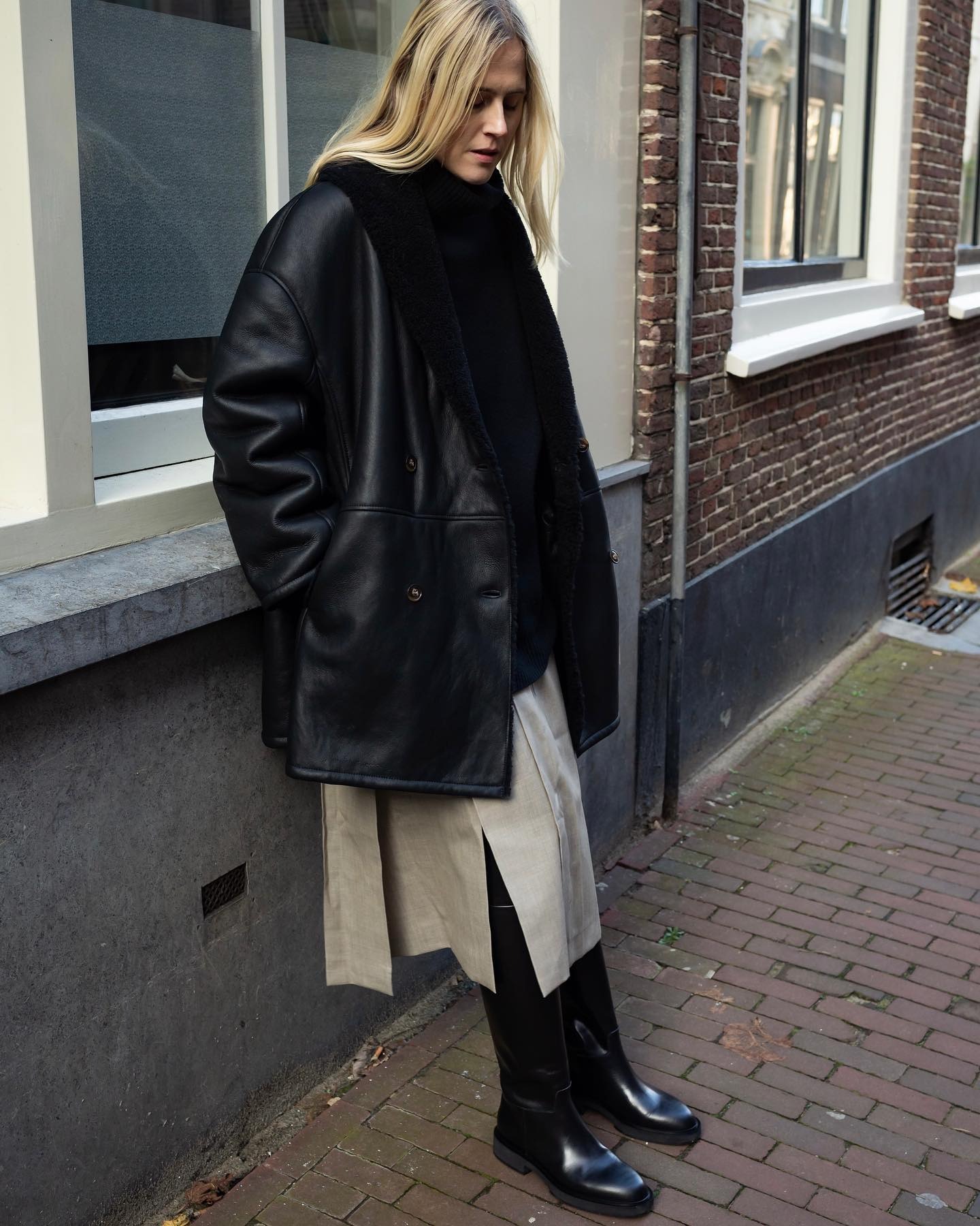 Influencer @lindatol_ wears a black sheepskin leather jacket with a suede skirt and black knee-high boots.