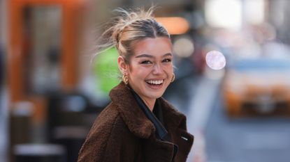 Millane Friesen is wearing a blue denim jeans, a grey hoodie and a brown long coat during New Yorker Fashion Week on February 15, 2022 in New York City