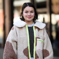 A smiley girl wears a pale blue long ruffled dress, a dark gray wool pullover, a beige and brown print pattern sheep zipper jacket