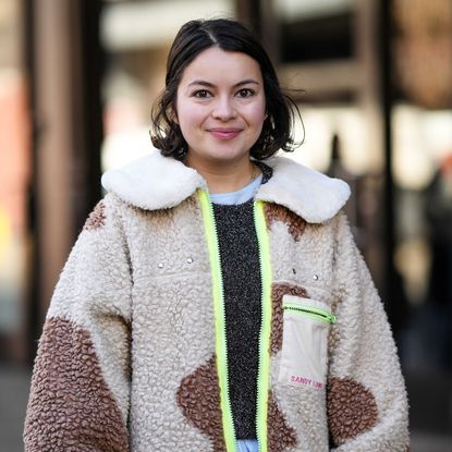 A smiley girl wears a pale blue long ruffled dress, a dark gray wool pullover, a beige and brown print pattern sheep zipper jacket