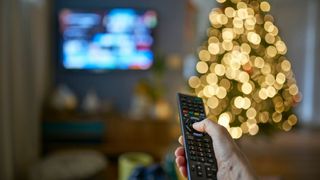 picture of woman pointing remote at TV with Christmas tree