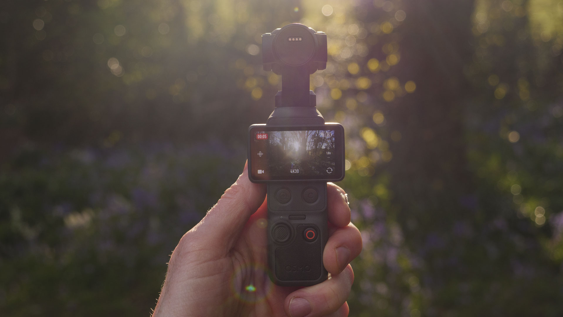 DJI Osmo Pocket 4 vlogging camera in the hand with natural background at golden hour