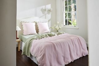 A white bedroom with lavender and light green bedding and pink pillows with a green scalloped edge