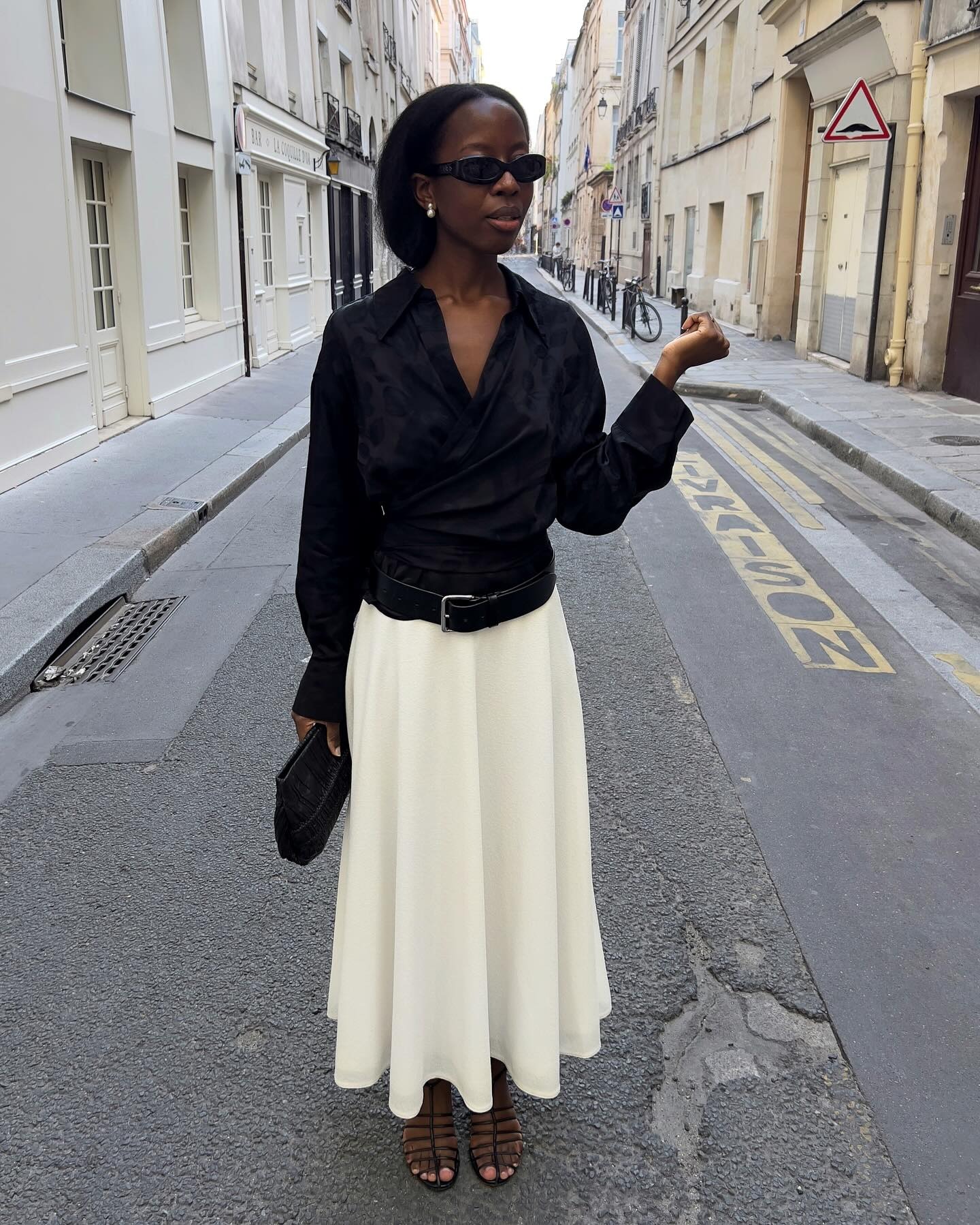 Influencer @sylviemus_ wears a black satin top with a white cream skirt and black caged heels.