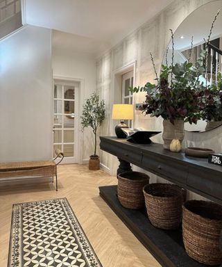 An entryway with a black wooden console table with baskets, white walls, and a black and white rug
