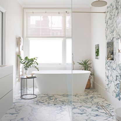 Elegant neutral bathroom with freestanding bath, plants and marble effect floor and wall tiles