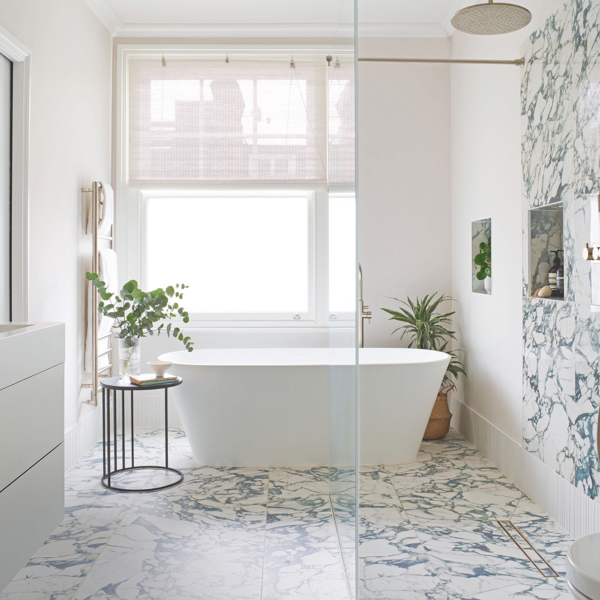 Elegant neutral bathroom with freestanding bath, plants and marble effect floor and wall tiles