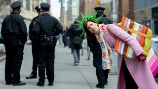 Elsbeth Tascioni (Carrie Preston), poses in a novelty Statue of Liberty hat behind NYPD officers while looking to camera in a promo image for CBS' Elsbeth