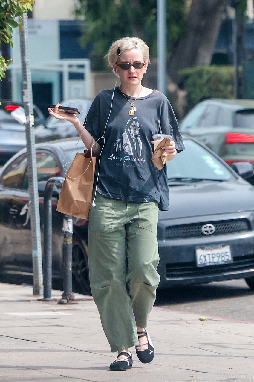 Julia Garner wearing a navy graphic tee, green barrel pants, and Puma ballet flats.