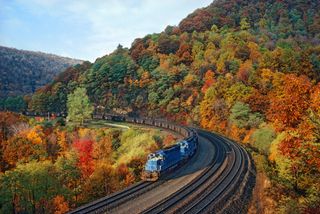 Blue train on tracks cutting through scenic Pennsylvania mountain range.