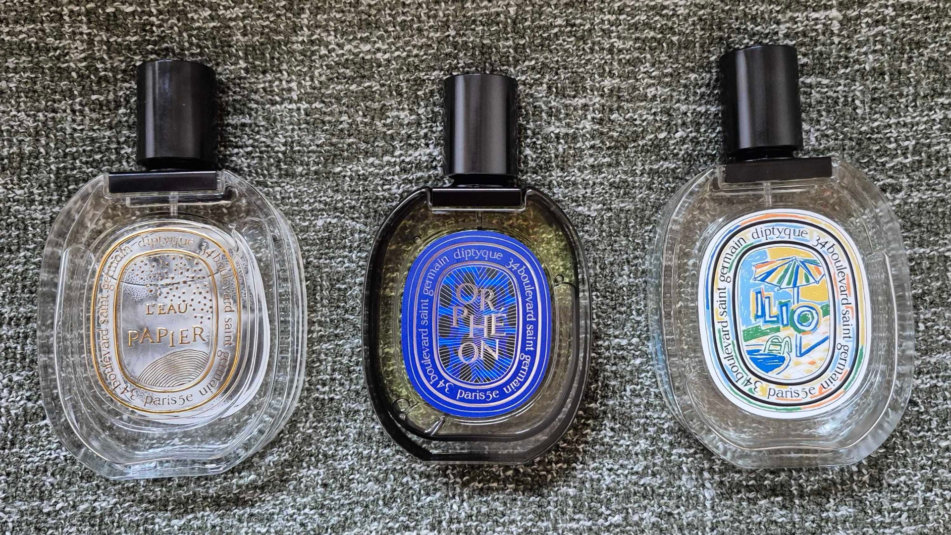 A photo taken by Digital Beauty Writer, Naomi Jamieson showing limited-edition bottles of Diptyque&#039;s L&#039;eau Papier, Orpheon and Ilio, laid out on a green blanket background