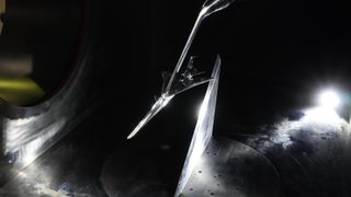 a long, narrow, silver model of an aircraft hangs from a boom in a dark concrete tunnel