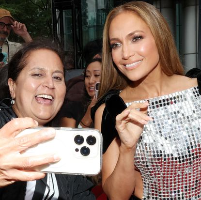 Jennifer Lopez wearing a silver dress and smiling for a selfie with a fan