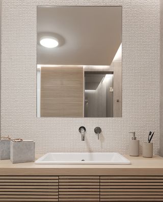 A vanity mirror on beige patterned wall above a rectangular shaped bathroom sink with embedded to a wooden base.