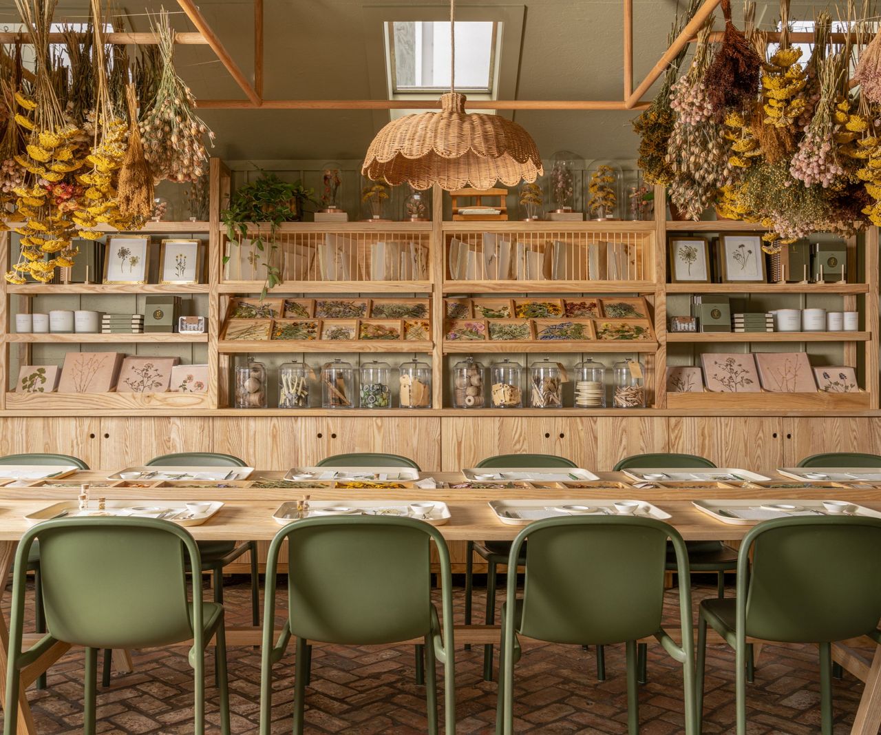 Room with brick floor, sage green painted walls, dried flowers hanging on ceiling, rattan light and long wood dining table with green chairs