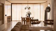 A warm beige living room with a couch, a pair of metal chairs, a tall floor lamp, a round dining table and chairs
