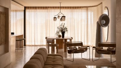 A warm beige living room with a couch, a pair of metal chairs, a tall floor lamp, a round dining table and chairs