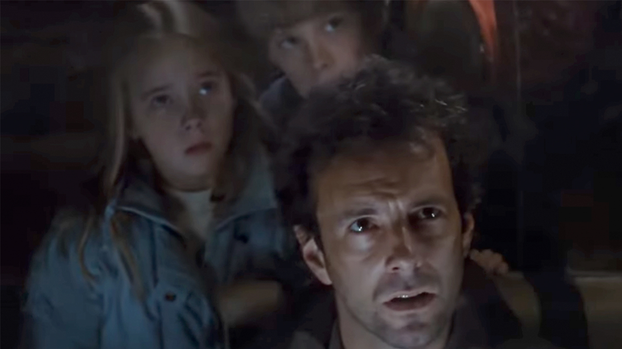 Two kids, including Newt, looking up from behind their father in Aliens