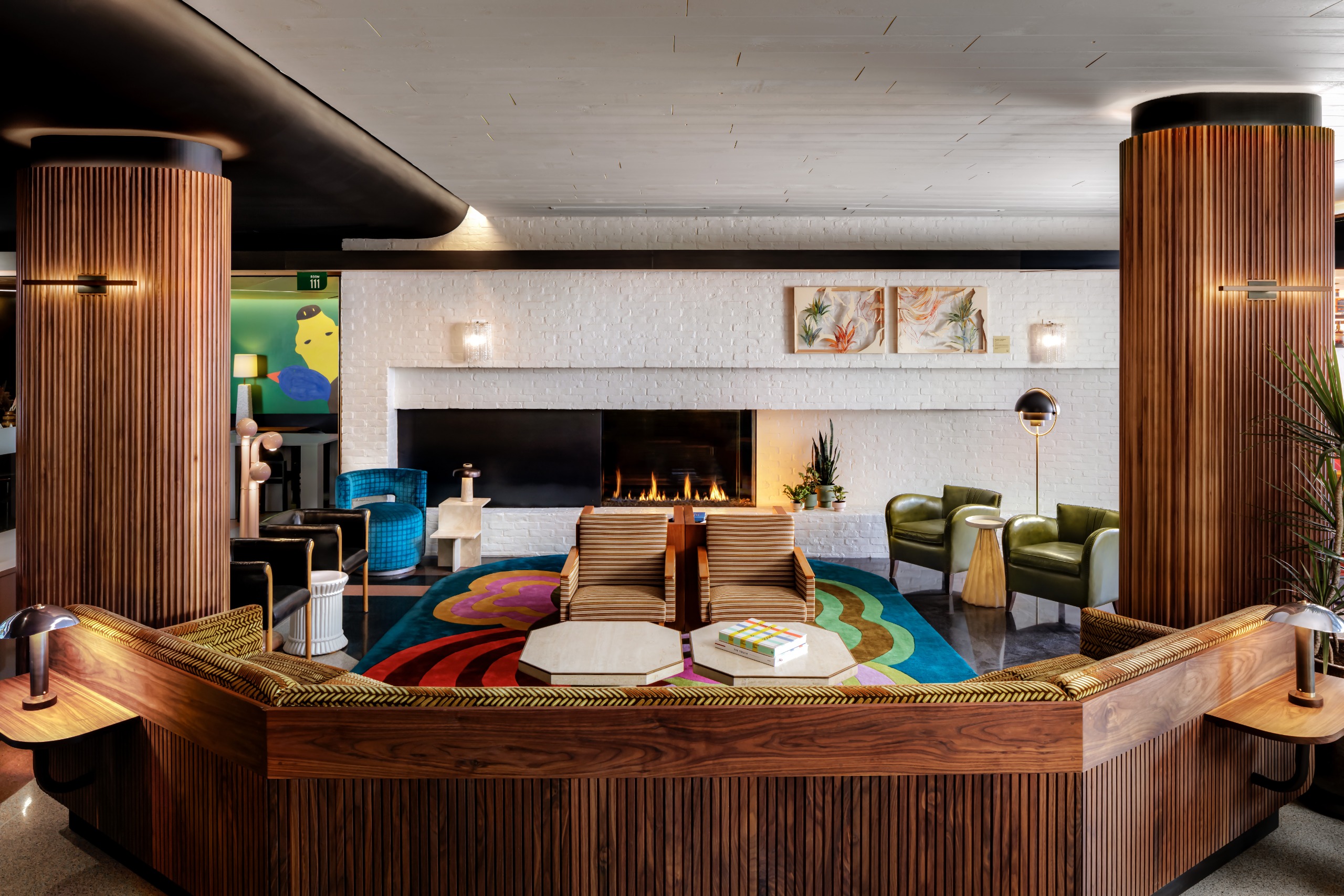 A hotel lobby carved from texture wood, with colorful rugs and artworks, white-washed walls, and a lit fire place.