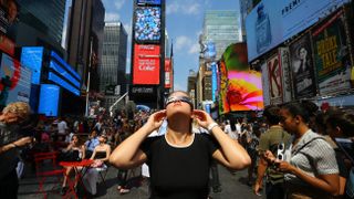 A woman wearing eclipse glasses looks up at the sky at the Times Square in New York City, United States on August 21, 2017.