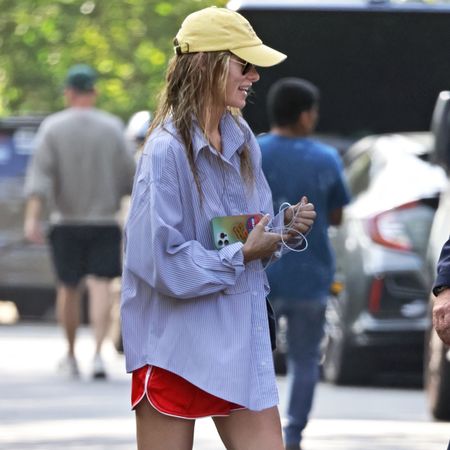 Olivia wilde wears red athletic shorts, a yellow baseball cap, and a button-down shirt.