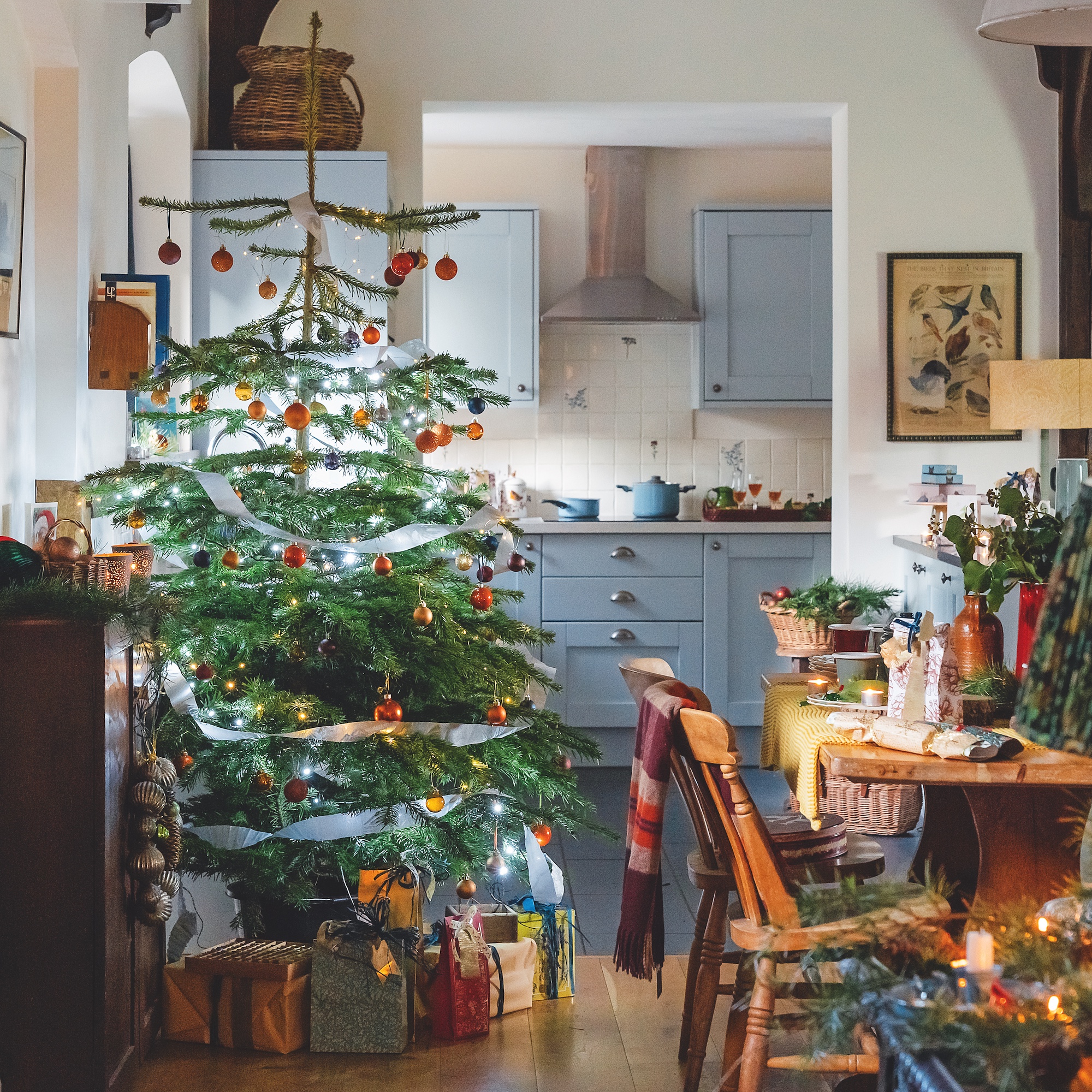 kitchen dining area with wooden farmhouse table and chairs with wooden kitchen cupboards painted pale blue, with christmas tree in the room