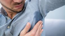 A close-up image of a man in a blue shirt touching a sweat patch under his armpit