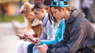 teens sitting outside look at their phones