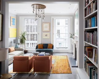 living room furniture arranging mistakes, apartment living room with yellow rug, focal pendant, small blue couch, two matching armchairs, bookcase, couch, artwork