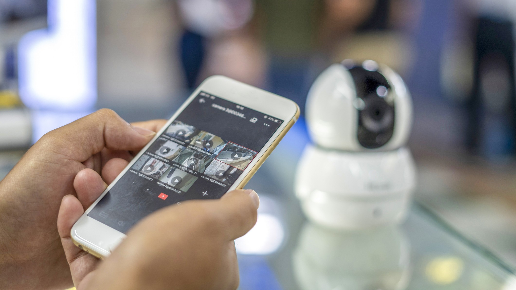 Person using home security smartphone app beside small indoor home security camera