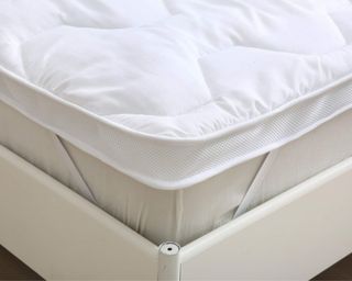 Mattress topper on bed secured with straps and styled with pillows