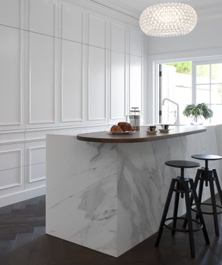 white hidden kitchen with marble island and black stools