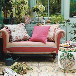 Orange striped chair in a green conservatory with a patterned tiled floor and potted plants