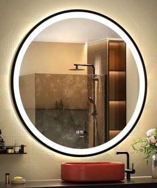 Round heated mirror on cream textured bathroom wall with red orange round feature sink below