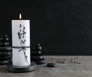 A single candle with lavendar wrapped around it and smooth dark stones