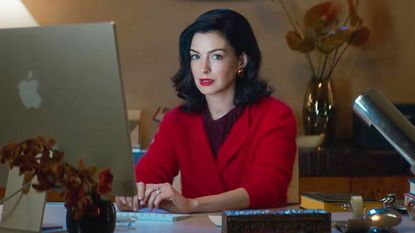 Anne Hathaway's Verity Crawford sitting at a desk and looking at the camera in Amazon's Verity film adaptation