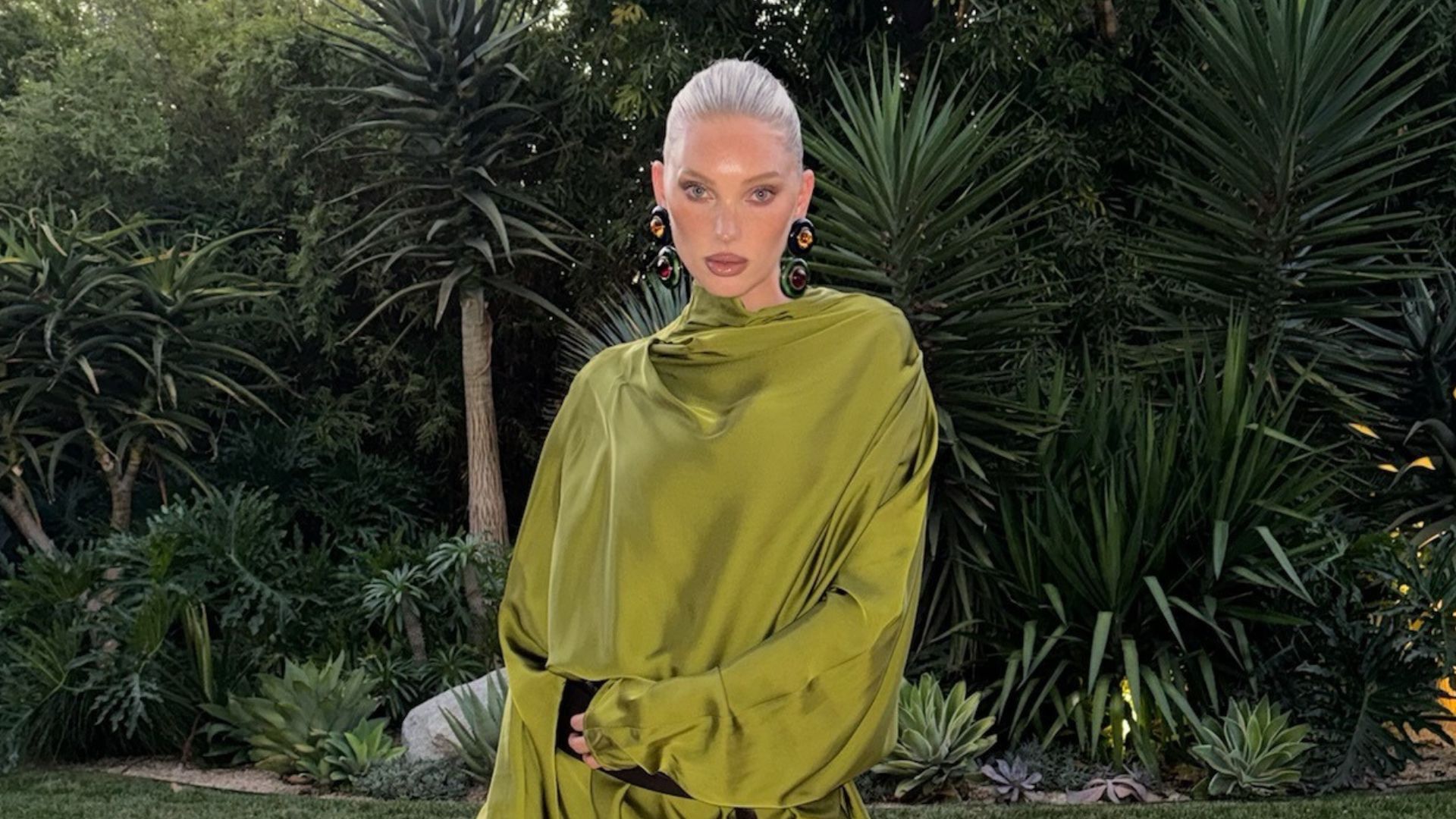 Elsa Hosk wears a green satin dress with a black woven bag and black mesh heels.