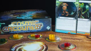 Cosmic Encounter box, cards, tokens, and playing pieces on a wooden table