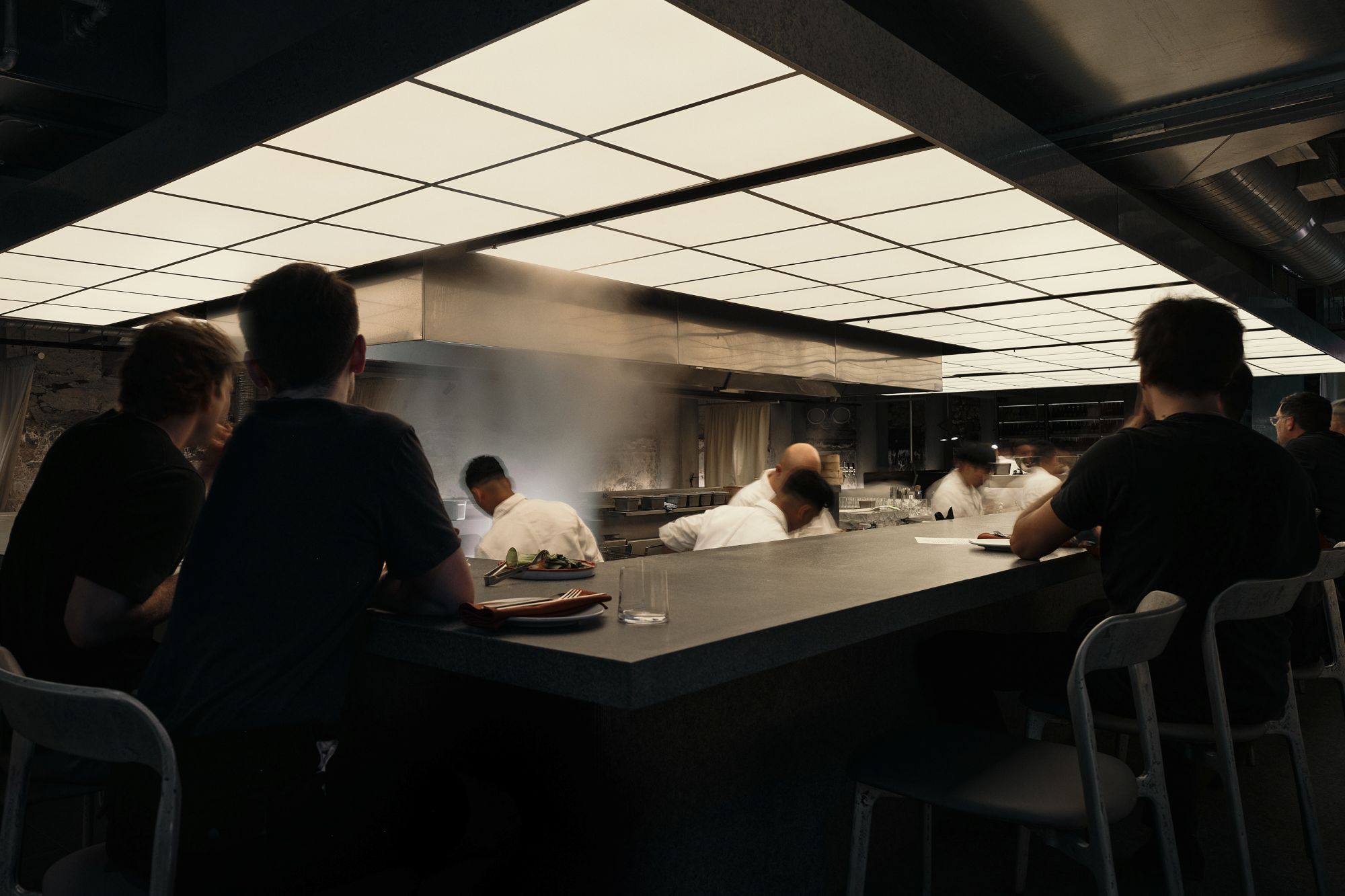 a restaurant bar counter with people sitting and chefs in the center cooking food
