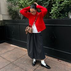 a woman wearing a red cardigan, white tee, black culottes shorts, and black loafers