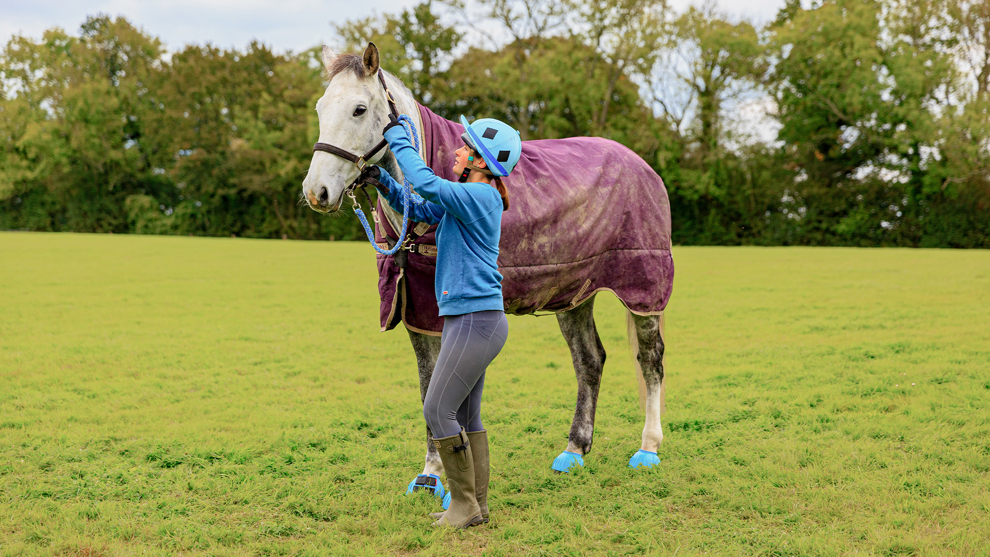 Woman undoing horse&amp;rsquo;s headcollar in a field to turn out