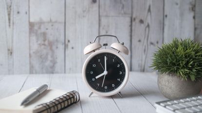 A white alarm clock beside a notepad and pen