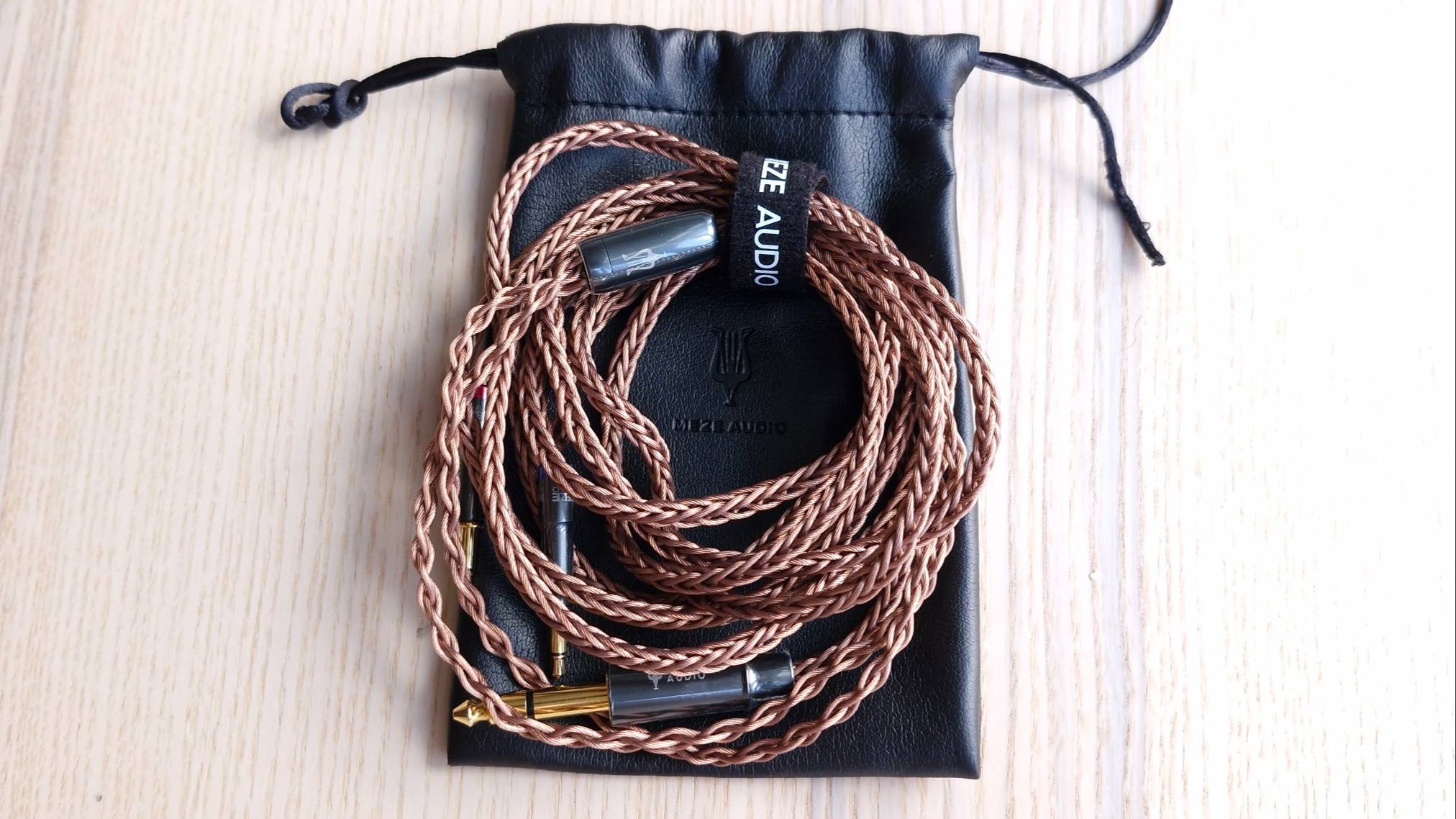 Cables, and leather case, for the Meze Audio Poet open-back over-ear headphones, on a wooden surface