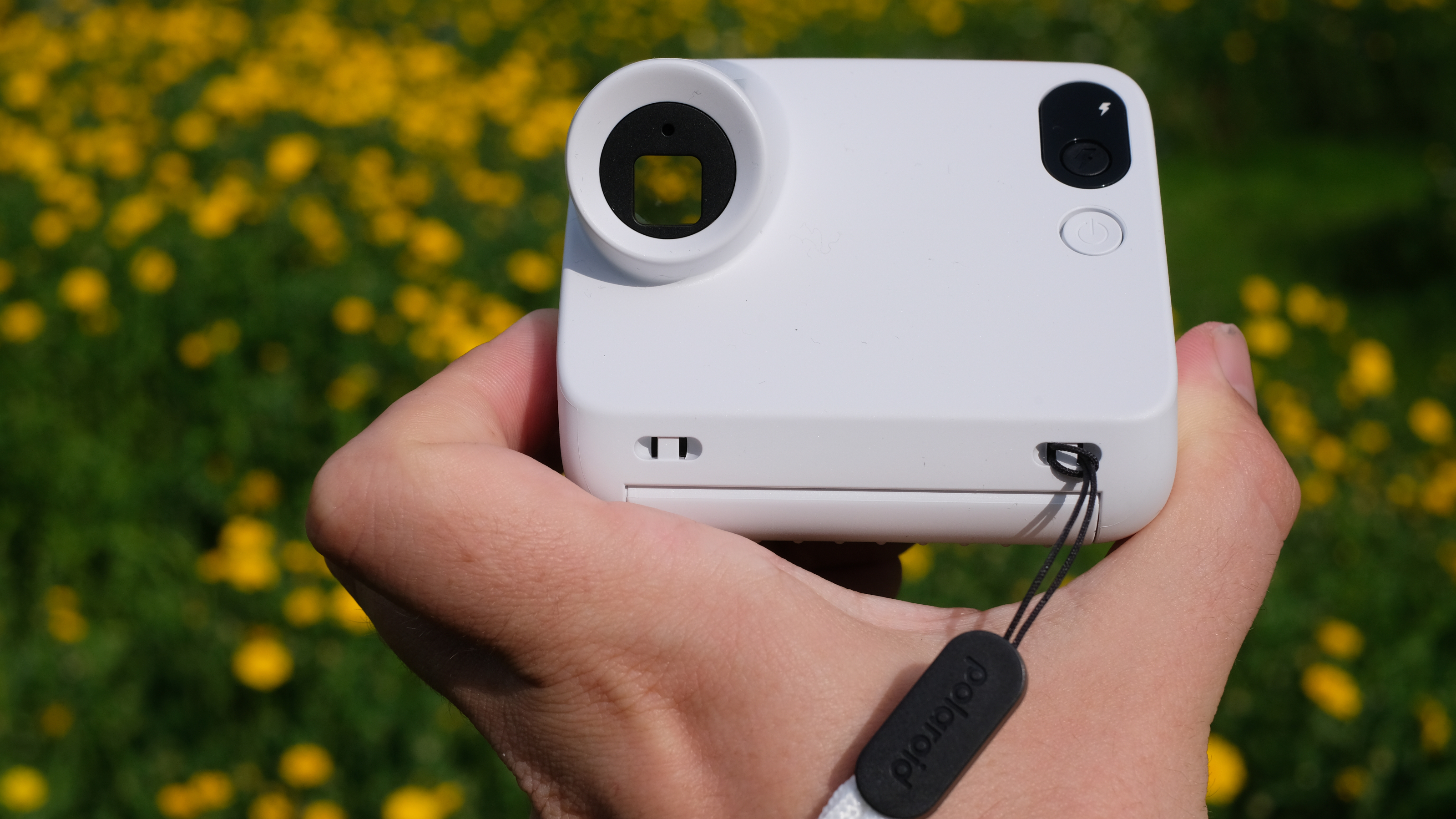 Photograph of man's hand holding Polaroid Go Gen 3 camera in white, rear view showing the view through the square viewfinder