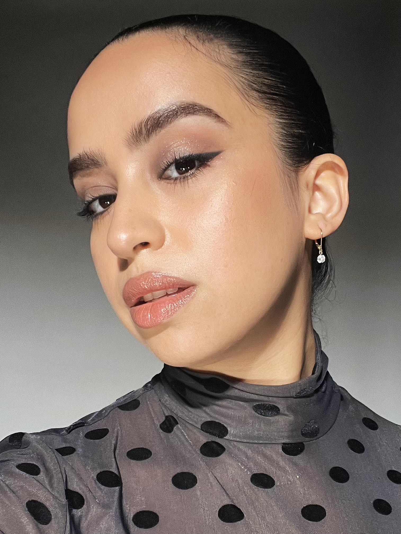a woman with a sheer black polka dot turtle neck shirt and winged black eyeline